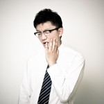 左手で頬を押さえている黒い眼鏡をかけた若い男性