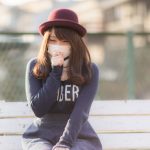 右手で咳を抑え、マスクをしている赤い帽子をかぶった若い女性