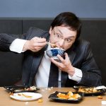 眼鏡をかけているサラリーマン風の男性が、ご飯をこぼしながら食べている様子